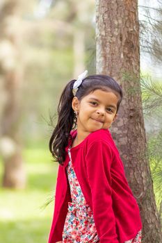 Little girl in flower dress and red sweater, very happy and smiling in the forest