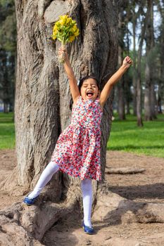 Little girl in dress celebrating in the park with a bouquet of flowers in her hand