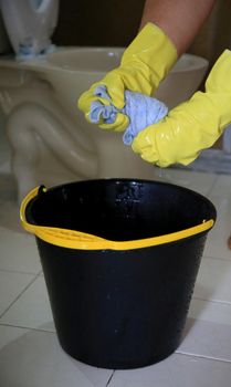 salvador, bahia, brazil - february 21, 2021: person wearing a rubber glove and holding a cloth next to a bucket while cleaning a bathroom in a residence in the city of Salvador.