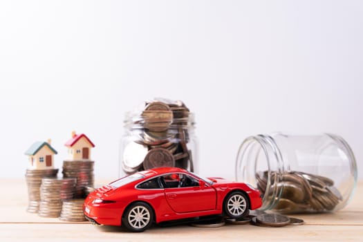 Jar full of coins with stack coin and red car on wooden table isolated grey background. Saving money and investment concept.