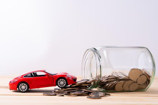 Jar of coins and red car on wooden table isolated grey background. Saving money and investment concept.