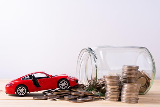 Jar of coins and red car on wooden table isolated grey background. Saving money and investment concept.