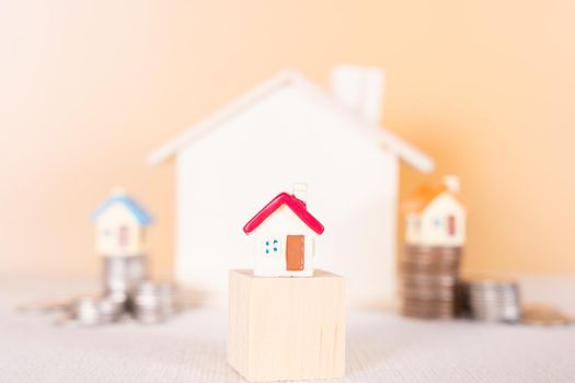 House on wooden block and stack coins isolated orange background. Saving money and investment concept.