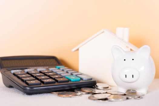 Piggy bank, calculator, coin and wooden house isolated orange background. Saving money and investment concept.