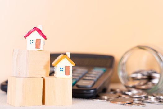 House on wooden block and coin inside jar and calculator isolated orange background. Saving money and investment concept.