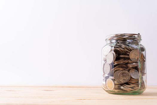 Jar full of coins on wooden table isolated grey background. Saving money and investment concept.