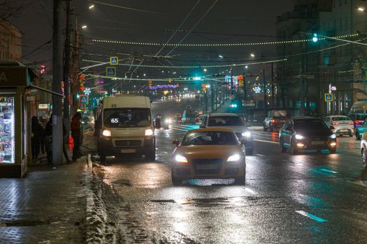 Tula, Russia - December 20, 2020: Night automobile traffic on wide city street and boarding passengers in a fixed-route taxi.