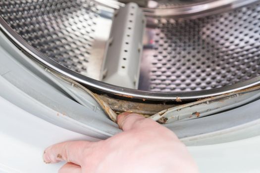 the hand protrudes the rubber band of the washing machine drum with a layer of dirt underneath.