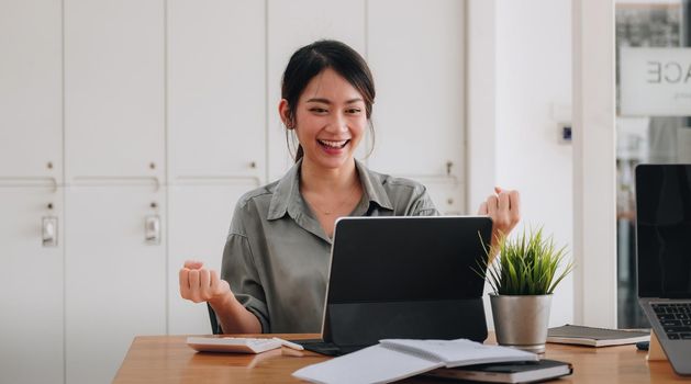 Portrait of an excited young asian girl using laptop computer and celebrating success for online learning or working at home.