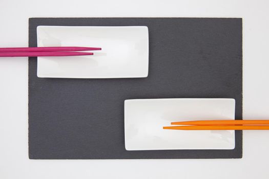 Rectangular slate plate with ceramic plate purple and orange chopsticks for sushi on the white table. Food Design.