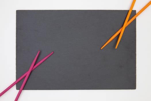 Rectangular slate plate with purple and orange chopsticks for sushi on the white table. Food Design.