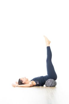 Restorative yoga with a bolster. Young sporty attractive woman in bright white yoga studio, lying on bolster cushion, stretching and relaxing during restorative yoga. Healthy active lifestyle.