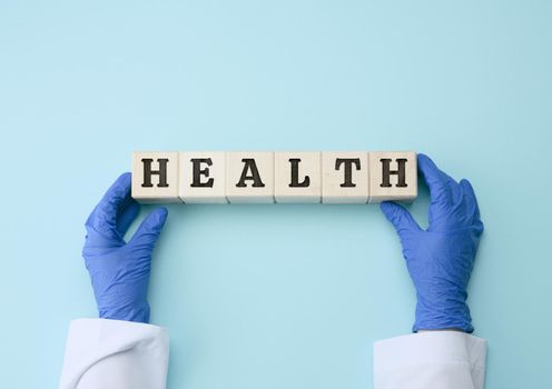 two female hands are holding wooden blocks with the inscription health on a blue background. Healthy lifestyle concept, help