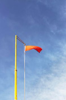 Red warning flag on a yellow flagpole against a blue and cloudy sky  seen from below