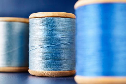 Three wooden spools of colored thread on  colored background , different shades of blue color  in every spool