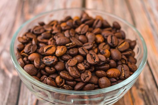 Freshly roasted coffee beans lie in a transparent glass vase on a wooden table