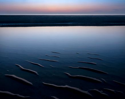 reflection of colorful sunset in water near beach on the dutch coast in holland