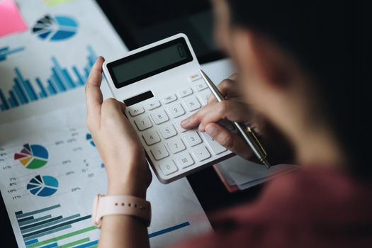 Above view of accouting woman consultant holding pen and using calculator with financial report on wooden desk at home. freelance, tax, accounting, statistics and analytic research concept.