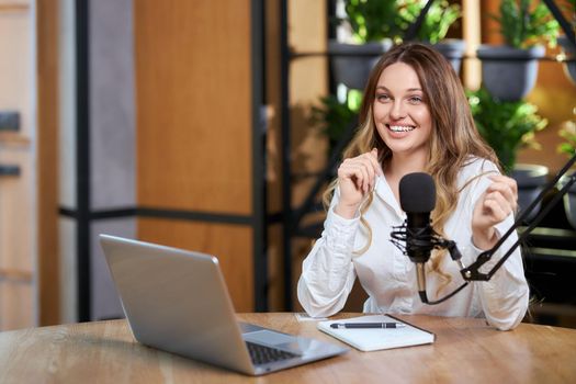 Close up portrait of happy young beautiful woman in white shirt talking about different topics with followers online by laptop. Concept of interview or live broadcast for subscribers. 