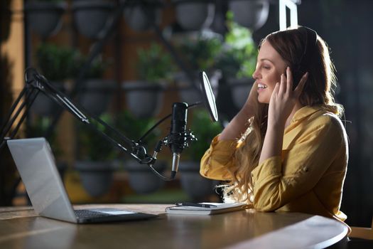 Side view of cute young attractive woman smiling and recording songs or interesting information for listeners. Concept of process recording songs with modern microphone and headphone.