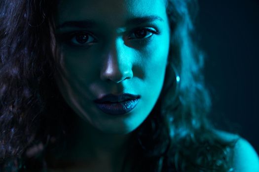 Close up portrait of attractive woman with trendy accessories and with curly hair looking at camera on dark blue light. Concept of professional shooting for glamour magazine. 