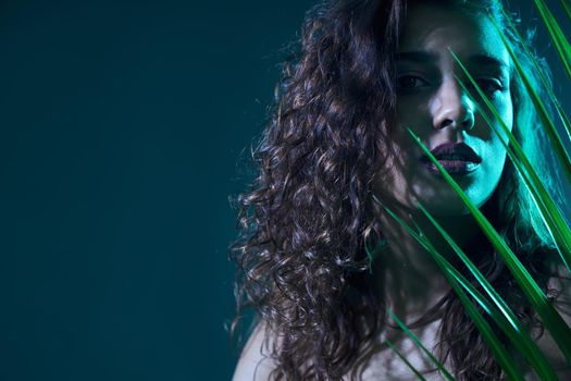 Close up portrait of beautiful woman with curly hair on shooting in green colors. Concept of professional studio in different style and colorful lights and accessories green leaf. 