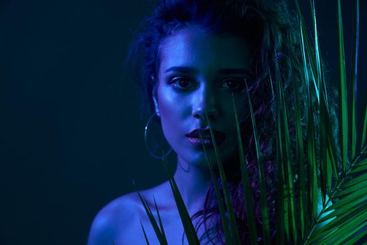 Fashion portrait of atrractive woman with modern green leaf accssesoies in professional studion with special dark blue lights. Concept of famous model on professional photo shoot. 