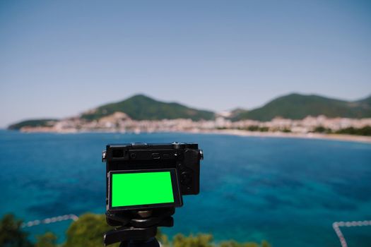 Black digital camera with an open display stands on a tripod against the backdrop of a mountain panorama. High quality photo