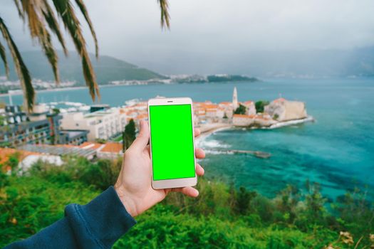 Man's hand holds a smartphone on the background of the old town of Budva Montenegro. Blank screen. High quality photo