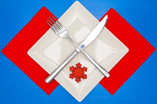 White square plate and red Christmas decoration on the blue wooden table.Top view.Flat Lay Image.