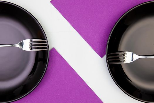 Black plates and purple napkins on the white wooden table.Top view. Flat Lay Image.