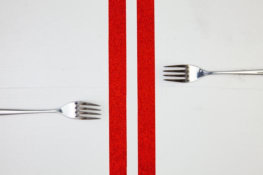Two forks and red ribbons on the wooden table.