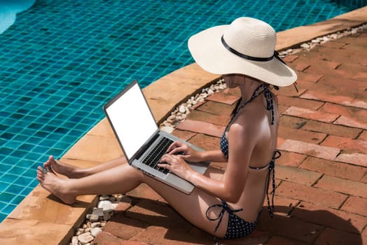 Asian Woman working on laptop computer sitting at poolside blue water