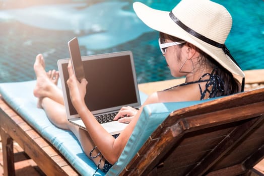 Portrait Beautiful Woman Sitting in deck chair and using laptop computer near swimming pool in vacation time blue water