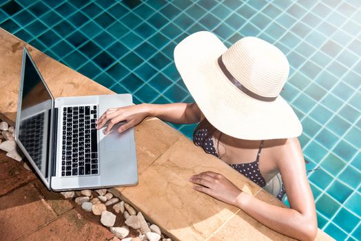 Beautiful smiling woman using laptop computer in swimming pool, blue water