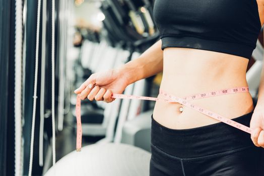 Beautiful woman using tape measuring waist, her is body slim after workout at fitness GYM