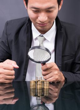 Businessman with magnifying glass looking With Stack Of Coins baht