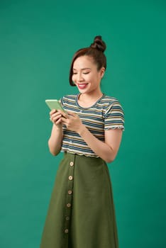 Portrait of a smiling casual woman holding smartphone over green background