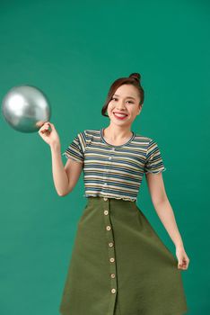 Happy smiling woman is looking on an air silver balloon having fun over a green background.