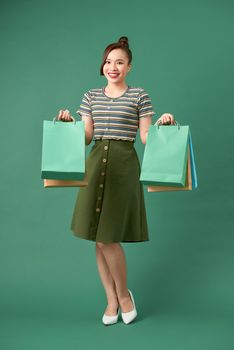 Beautiful young asian woman with colored shopping bags over green background