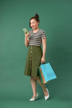 cheerful elegant girl holding shopping bags while chatting on smartphone on green background