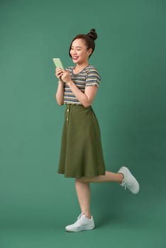 Full length image of attractive woman in casual clothing using mobile phone over green background