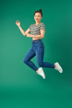 Happiness, freedom, motion and people concept - smiling young woman jumping in air over green background.