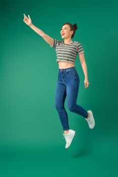 Full length of cheerful young Asian woman or teenage girl jumping in air over green background.