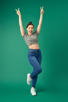 Full-length portrait of a joyful attractive Asian girl celebrating success while jumping over green background.