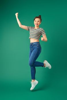 Portrait of happy positive young Asian woman jumping and waving hand over green background.