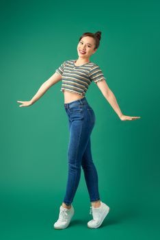 Full length portrait of happy young Asian woman standing on one leg and dancing on green background.