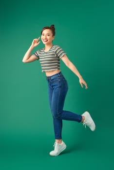 Full-length portrait of a happy young woman dancing on green background