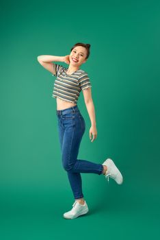 Joyful young Asian woman standing on one leg. Full length view of blissful girl dancing on green background.