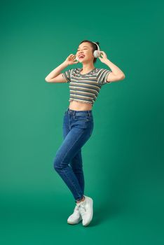 Energy girl with headphones listening to music with closed eyes on green background in studio. Wearing T-shirt, jeans.
